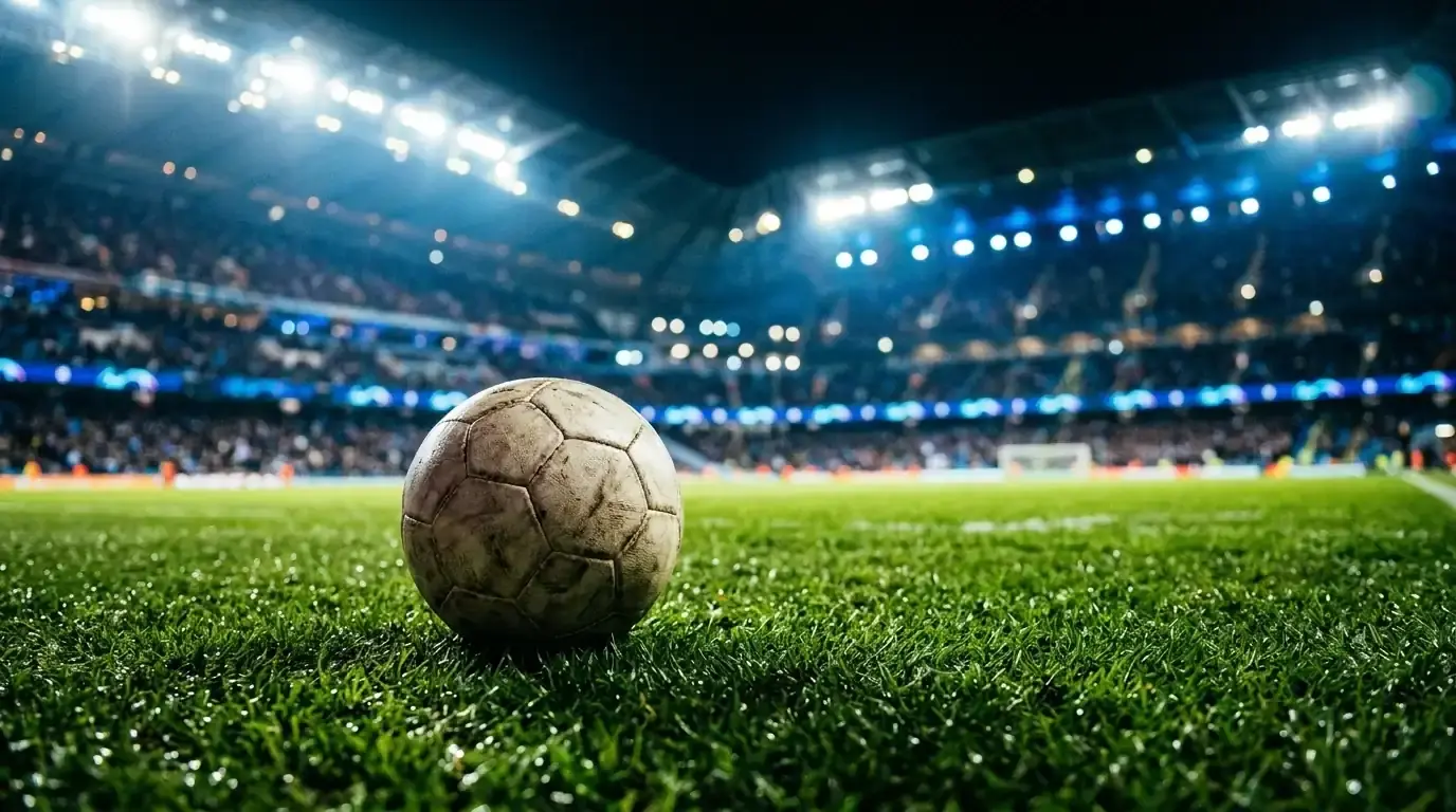 Dettaglio di un pallone da calcio sul terreno illuminato di uno stadio, tribune sfocate sullo sfondo