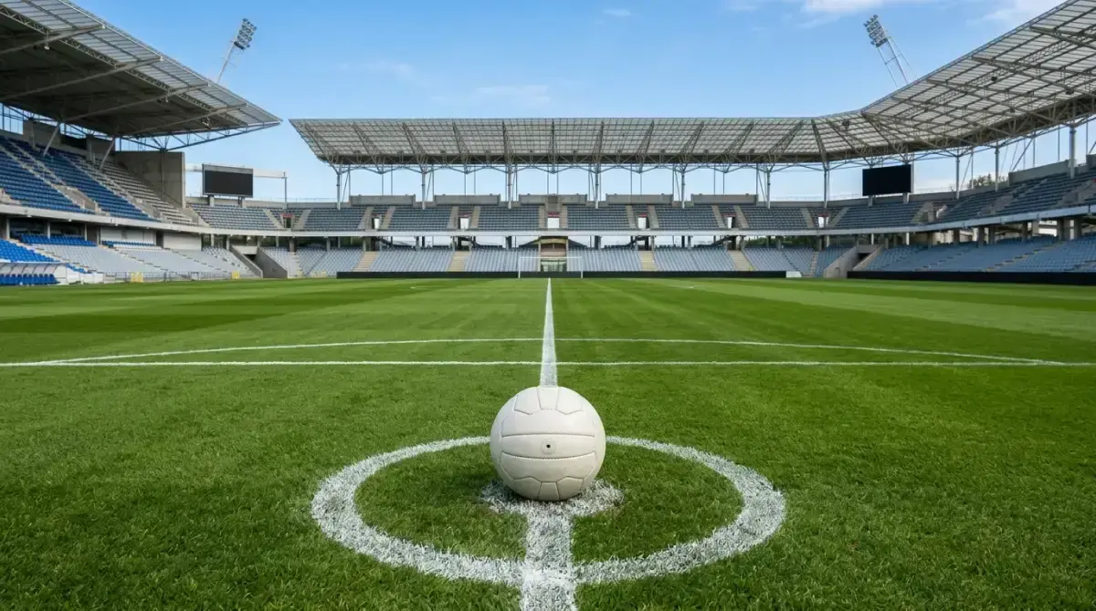 Pallone fermo sul dischetto del centrocampo in uno stadio illuminato a giorno, cielo sereno, campo verde perfetto poco prima del fischio d'inizio